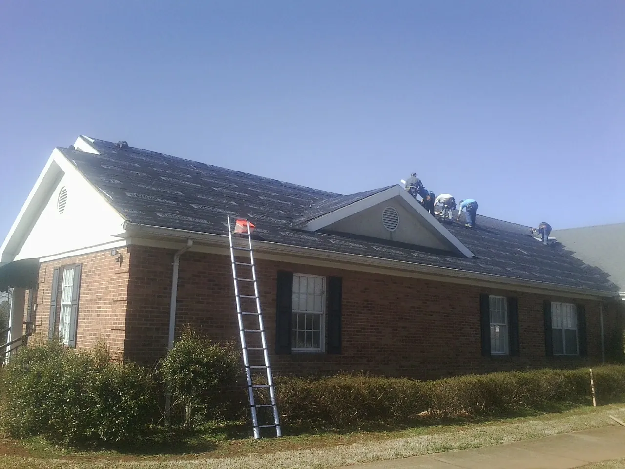 Crew tearing shingles off a brick ranch roof with a ladder set — Metal Roof Repair work by our crew in Paxinos