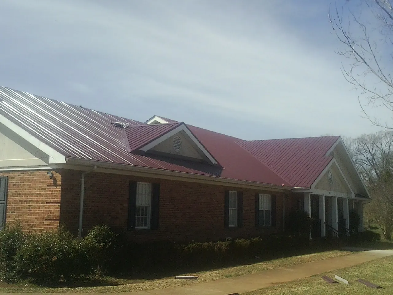 Red metal roof with gabled entries on a long brick building, from a Hail Damage Roof Repair job in Paxinos