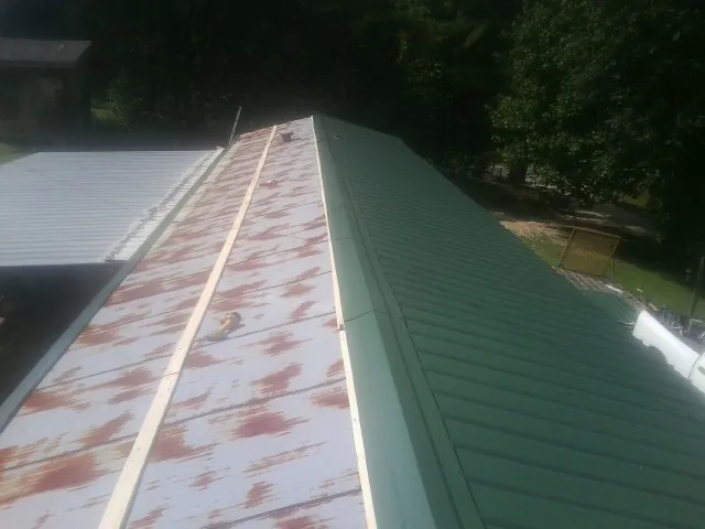 Old rusted panels beside newly installed green metal roofing — Wind Damage Roof Repair by Roofing Brothers in Paxinos
