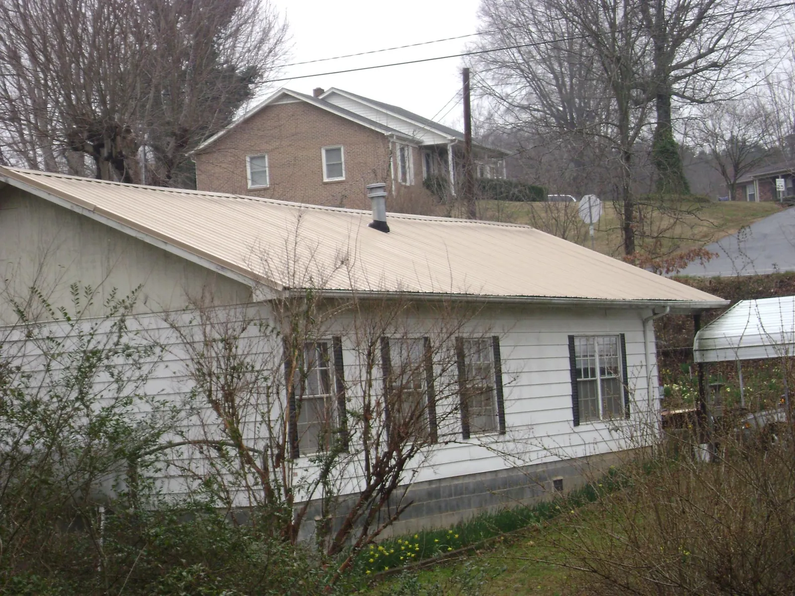 Tan metal roof on a white sided house set into a hillside — Commercial Roofing by Roofing Brothers in Paxinos