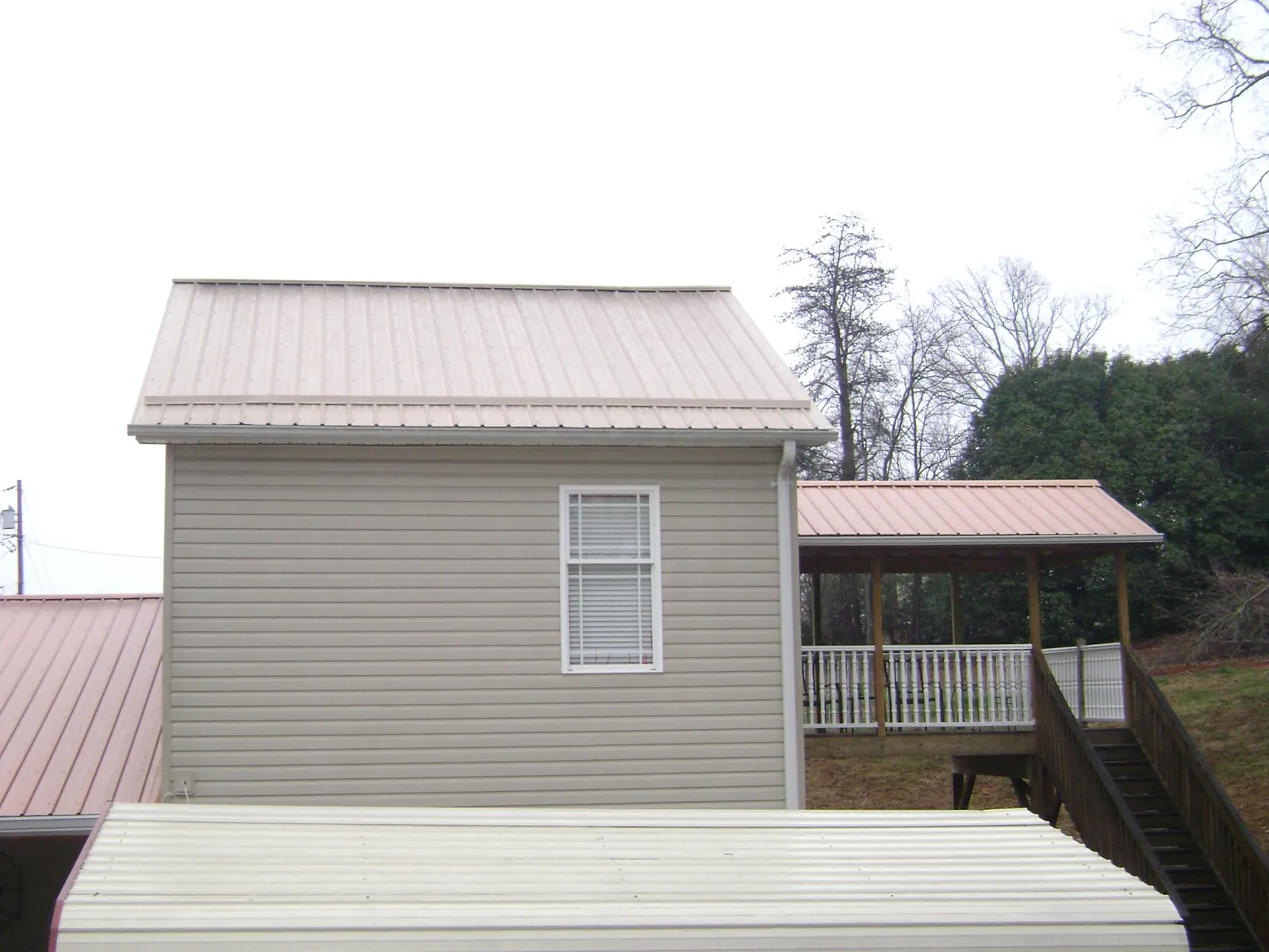 Tan metal roofs on a two story addition and attached porch, from a Roof Replacement job in Paxinos